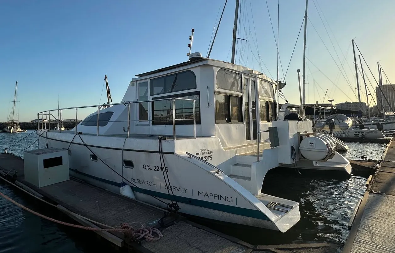 Vaquita at her berth, starboard-stern view with the wheelhouse, tender lashed on deck, and the marina behind.